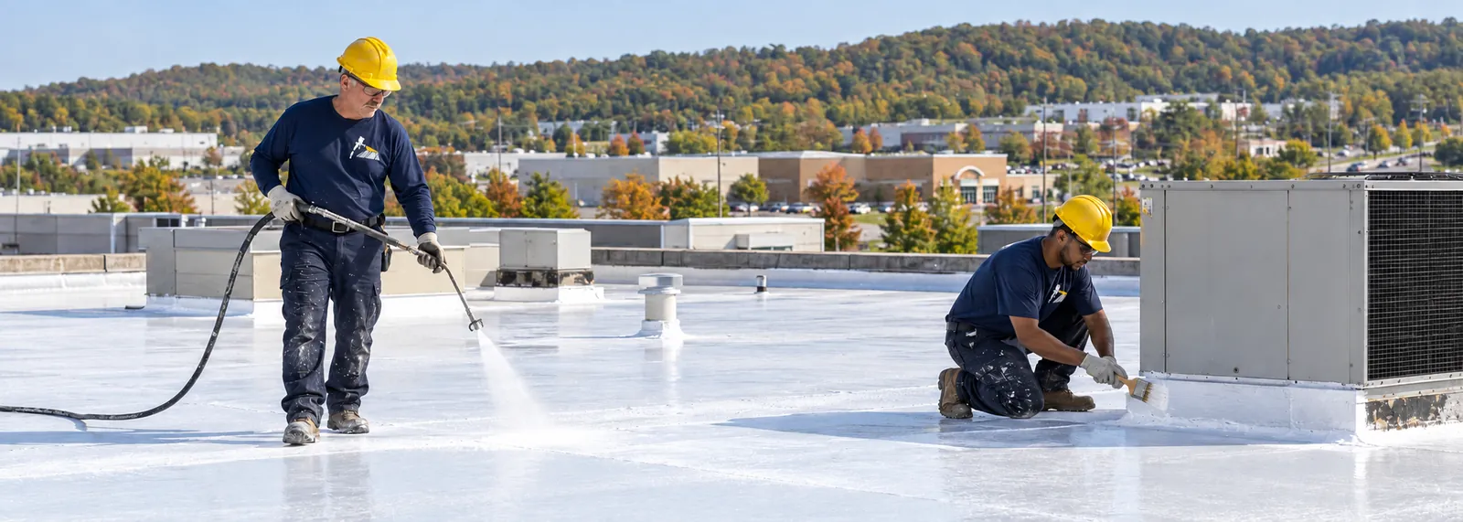 Crew spraying white silicone coating beside a rooftop unit on a flat commercial roof